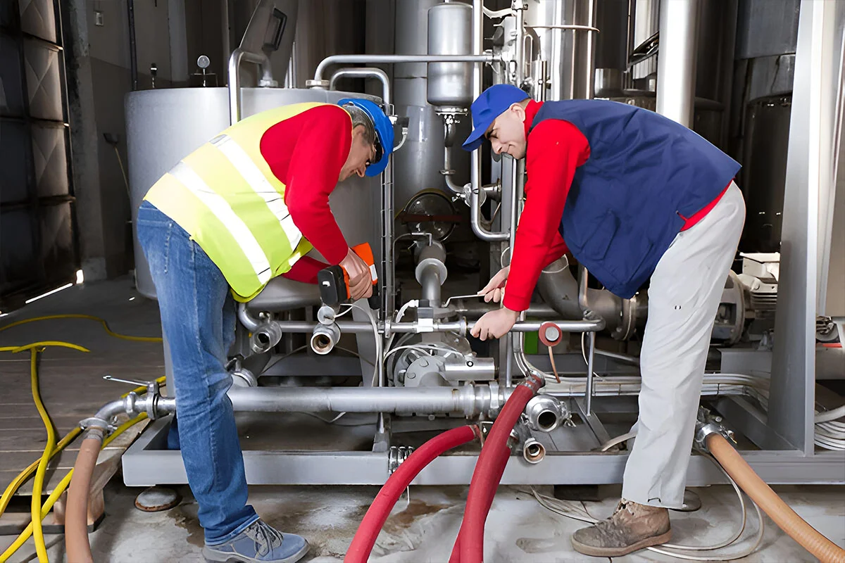 Two technicians installing pipework and hose connections on a boiler skid