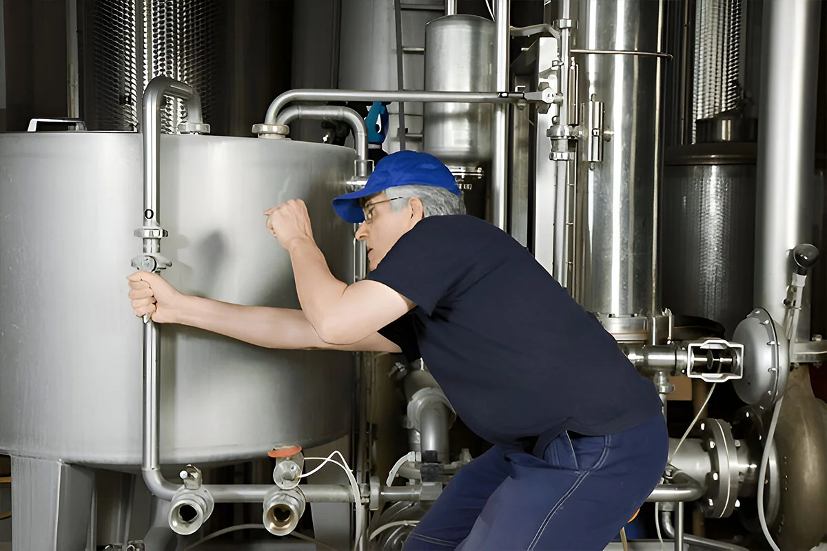 Technician operating a valve on a stainless steam vessel in a plant